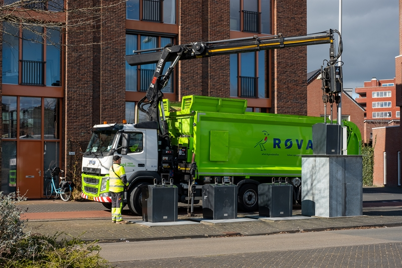 Een medewerker van de vuilnisophaaldienst bedient de mechanische grijparm van een vuilniswagen om een ondergrondse vuilcontainer te legen. 